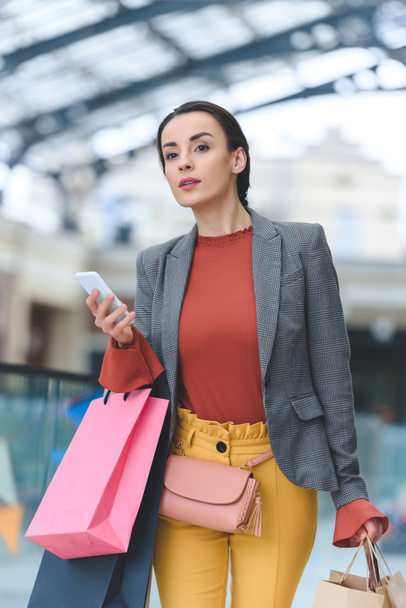 attractive woman walking with shopping bags and smartphone in mall - Foto, Imagem