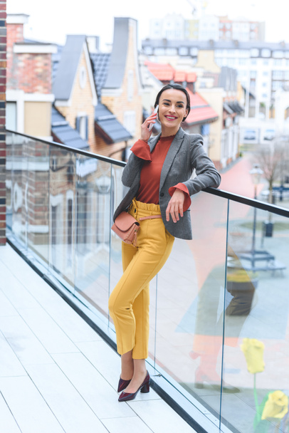 beautiful stylish woman standing on balcony and talking by smartphone - Foto, afbeelding