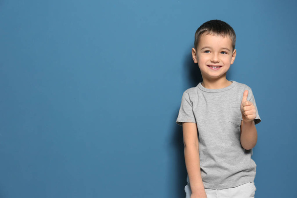 Χαριτωμένο μικρό αγόρι που δείχνει thumbup χειρονομία σε χρώμα φόντου - Φωτογραφία, εικόνα