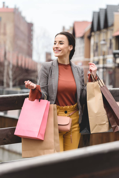 smiling attractive woman standing with shopping bags on bridge - Photo, Image