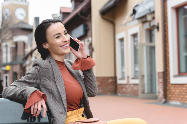 smiling beautiful stylish woman talking by smartphone on bench - Zdjęcie, obraz