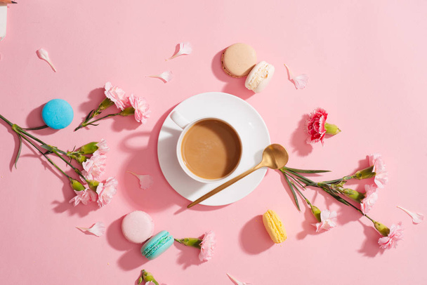 Acogedor desayuno de la mañana. Macarrones de color, flores y taza de café sobre fondo rosa
 - Foto, Imagen