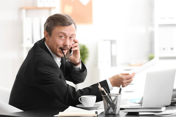 Mature man talking on phone while working indoors - Fotó, kép