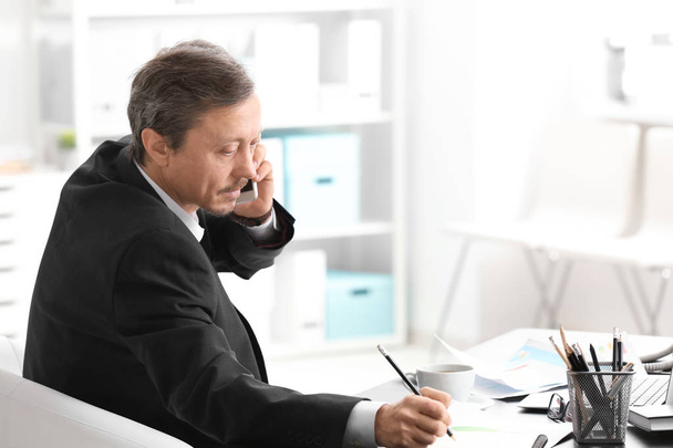 Mature man talking on phone while working indoors - Fotografie, Obrázek