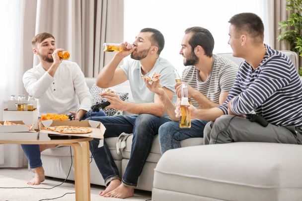 Young men drinking beer and eating pizza while playing video games at home - Photo, image