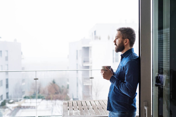 A man by the window holding a cup of coffee at home. - Photo, Image