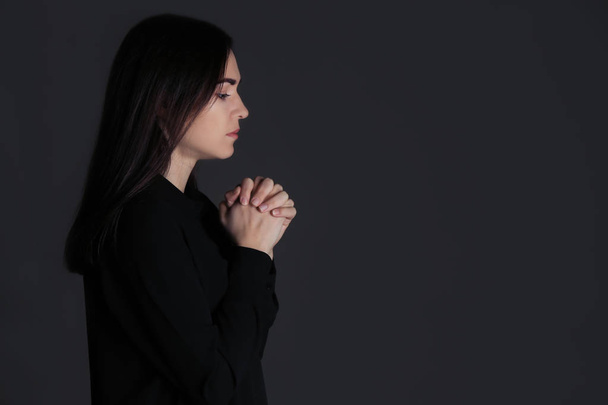 Religious young woman praying on dark background - Foto, Imagen