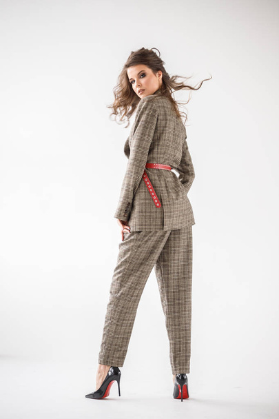 Fashion studio portrait of beautiful curly woman wearing checkered casual suit with red belt, standing on white wall background  - Фото, зображення