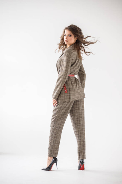 Fashion studio portrait of beautiful curly woman wearing checkered casual suit with red belt, standing on white wall background  - Foto, Imagem