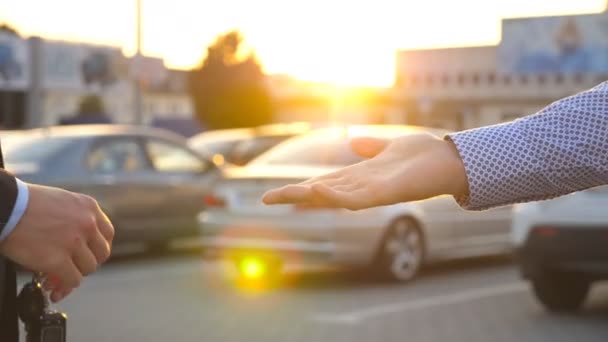 Mannelijke handen in pak het geven van de sleutels van de auto naar zijn vriend met mooie zon flare op achtergrond. Arm van zakenman passeert auto sleutel. Handdruk tussen twee zakenmannen buiten. Close-up van Slow motion - Video
