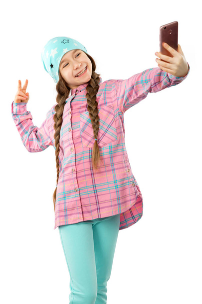 Porträt eines lächelnden kleinen Mädchens, das sein Handy in der Hand hält und ein Selfie auf weißem Hintergrund macht - Foto, Bild