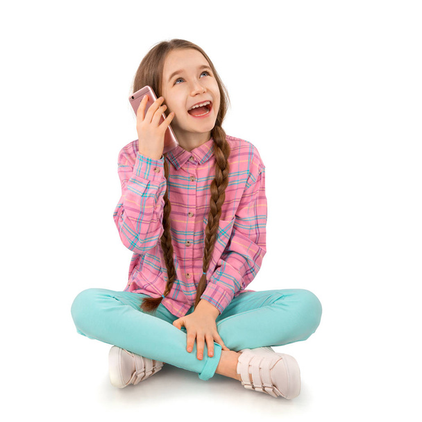 Счастливая маленькая девочка со смартфоном, сидящая на полу на белом фоне. Люди, дети, технологии
 - Фото, изображение