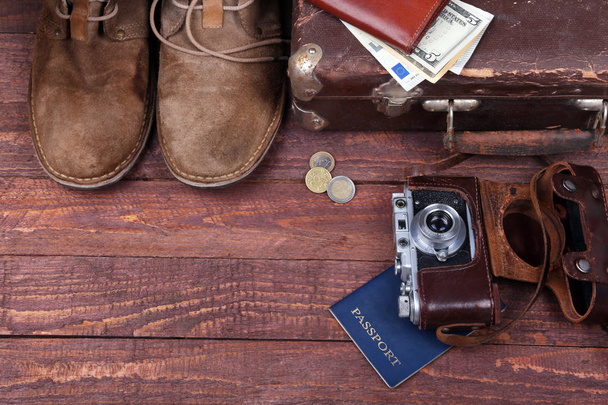 Travel concept with Vintage suitcase, sunglasses, old camera, suede boots, case for money and passport on wooden floor. - Photo, image