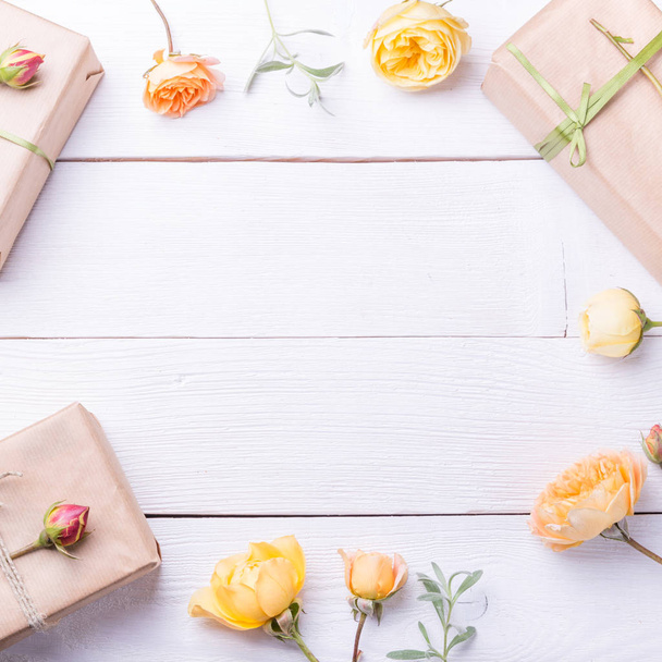 Flowers composition. Gifts and rose flowers on white wooden table. Women Day. Flat lay, top view - Photo, Image