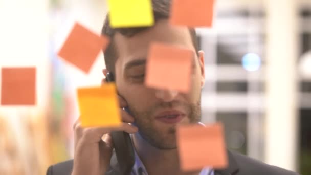 Business man making a mobile meeting with sticky note schedule on window - Séquence, vidéo