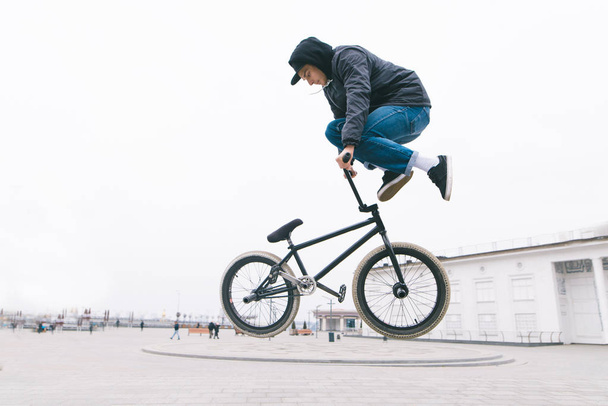 BMX freestyle. BMX fietser maakt complexe trucs op een fiets. Jonge man maakt spectaculaire stunts tegen de achtergrond van het stadsplein. - Foto, afbeelding