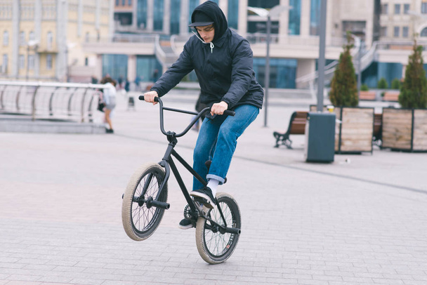 The teen does tricks on the BMX. BMX cyclist rides a bike around the park and makes tricks. BMX concept - Foto, Imagen