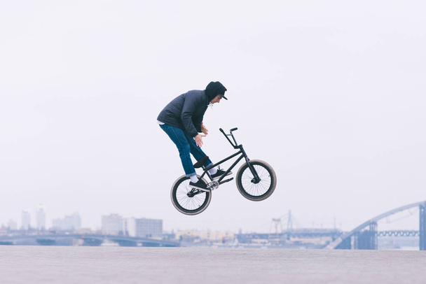 The Young BMX reader makes the Barzpin trick against the background of the city skyline. BMX concept. Tricks on the minimalist background.BMX freestyle - Photo, Image