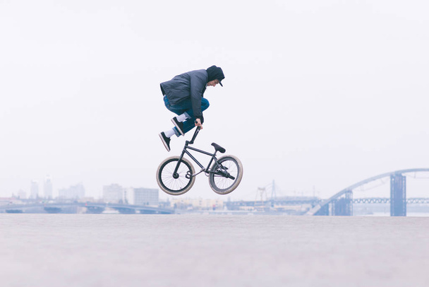 Joven lector de bicicletas BMX hace trucos en el aire contra el fondo del paisaje urbano. BMX freestyle. Cultura callejera
 - Foto, Imagen