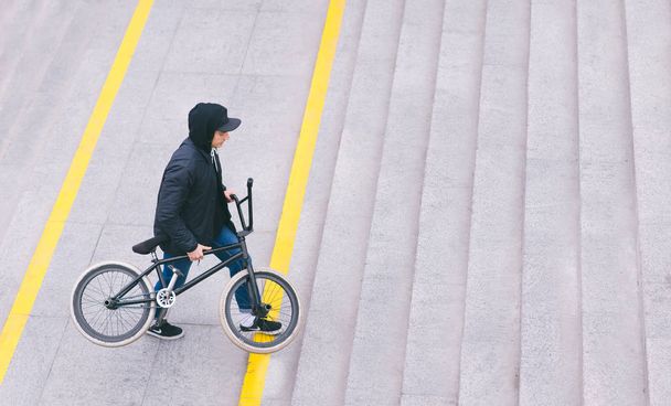 Ein stylischer junger Mann klettert mit einem Fahrrad in der Hand auf eine Leiter. Spaziergang mit dem Fahrrad. bmx Konzept. Straßenkultur - Foto, Bild