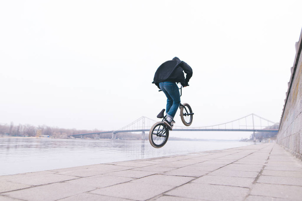 Стильный мужчина делает трюки на велосипеде BMX на открытом воздухе. Фристайл на bmx. На набережной
 - Фото, изображение