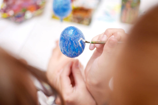 Child hands painting blue easter egg with white lines - Foto, afbeelding