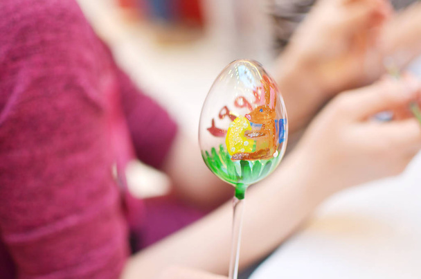 Το παιδί στα χέρια ζωγραφική γυαλιού Πασχαλινό αυγό με πολύχρωμα κουνέλι - Φωτογραφία, εικόνα