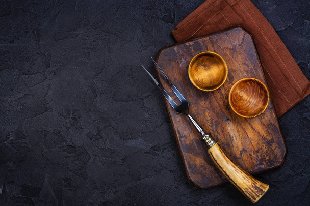 Placa de corte de madeira, tigela para especiarias e garfo vintage e faca sobre pedra fundo preto
 - Foto, Imagem