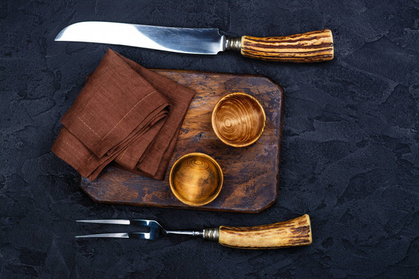 Wooden cutting board, bowl for spices and vintage fork and knife on stone black background - Foto, Imagem