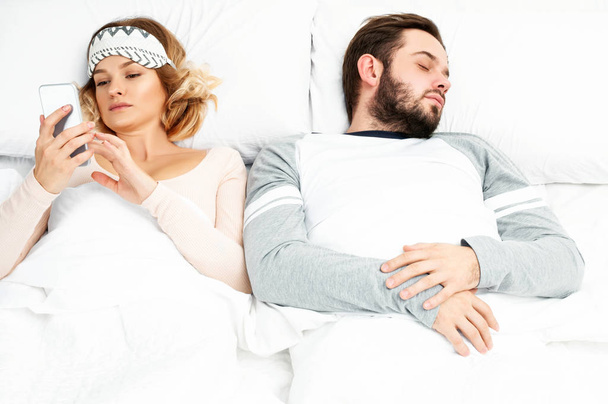 Young woman using smartphone while her husband is sleeping - Foto, Bild
