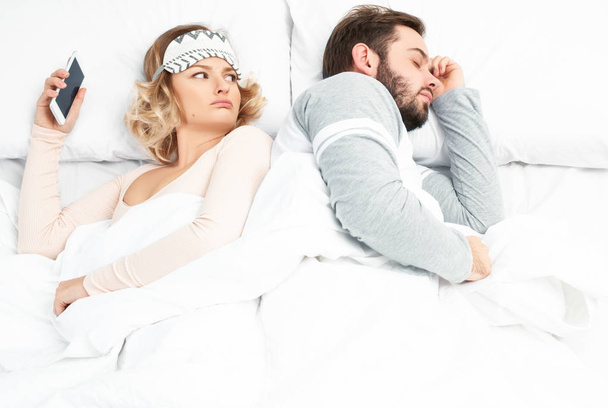 Young woman using smartphone while her husband is sleeping - Фото, зображення