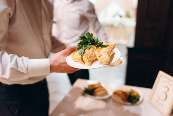 Обрізаний вид офіціантів, що приносять білі тарілки зі смаженими пирогами
 - Фото, зображення