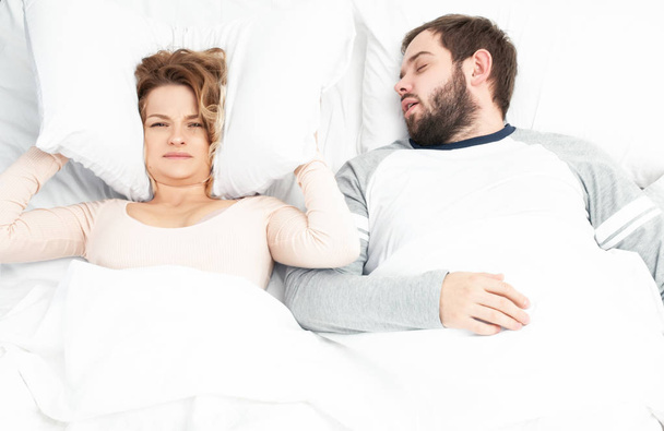 Man snoring and woman can't sleep, covering ears with pillow for snore noise - Foto, Imagen