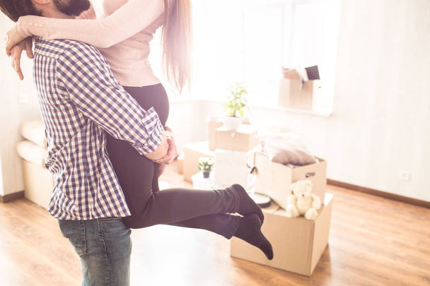 Close up of young couple in a bright room. Young man is holding his wife on the hands. There are boxes with different stuff on the floor. - Fotoğraf, Görsel