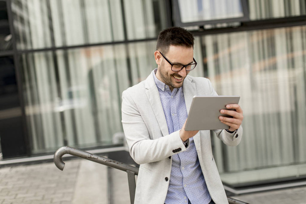 Handsome young businessman with digital tablet by the office building - Photo, Image