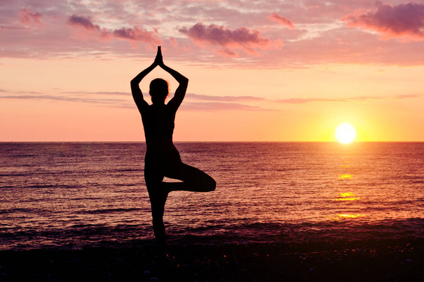 Frau bei Sonnenuntergang praktiziert Yoga. Küste, Silhouette - Foto, Bild