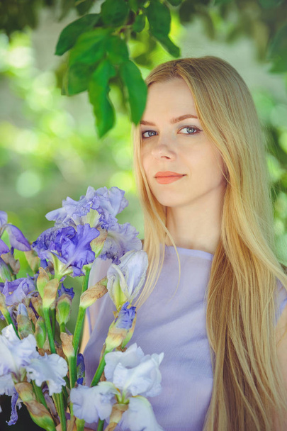 Jolie jeune fille aux cheveux blonds enfantés et au maquillage naturel sentant l'iris bleu violet sur un fond extérieur, tendresse et douceur sur fond de nature
 - Photo, image