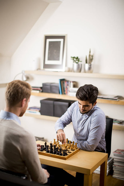 Two young men playing chess in room - Fotó, kép