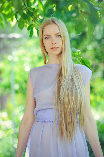Attractive modest young girl with blond dren hair and natural make-up in purple dress outdoors, tenderness and softness on nature background - Foto, immagini