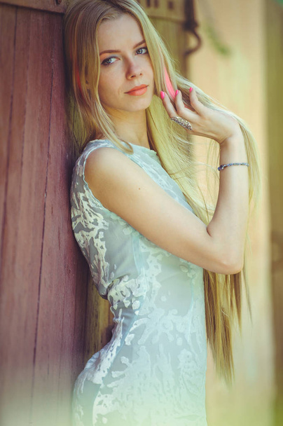 Attractive modest young blond woman playing with hair on red wooden background her hair painted in pink striped striped, in blue dress shy and inquisitive - Fotó, kép