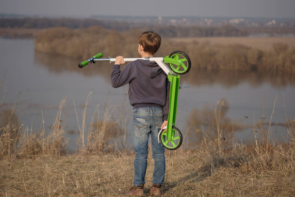 Europejskiego chłopiec z skuter na wysokim brzegu rzeki - Zdjęcie, obraz
