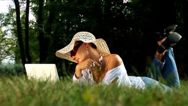 Jovem mulher deitada no parque usando computador portátil
 - Filmagem, Vídeo