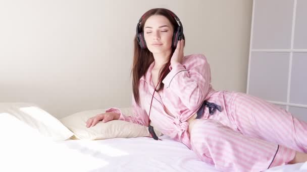 woman in pajamas on the bed dances to music from headphones - Footage, Video