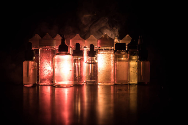 Концепція вейпу. Димові хмари та вейп-рідкі пляшки на темному тлі. Світлові ефекти
 - Фото, зображення