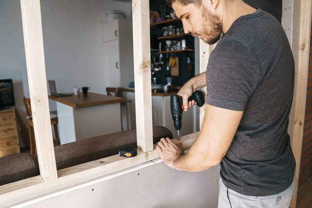 Чоловік з викруткою в руці фіксує дерев'яну конструкцію для вікна в своєму будинку. Ремонтувати самостійно
. - Фото, зображення