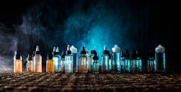 Vape concept. Smoke clouds and vape liquid bottles on dark background. Light effects. Useful as background or vape advertisement or vape background. - Photo, Image