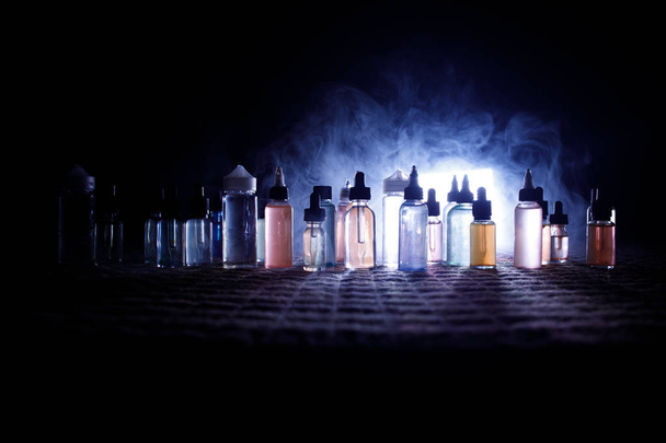 Vape concept. Roken wolken en vape vloeibare flessen op donkere achtergrond. Lichteffecten. Nuttig als achtergrond of vape advertentie of vape achtergrond. - Foto, afbeelding