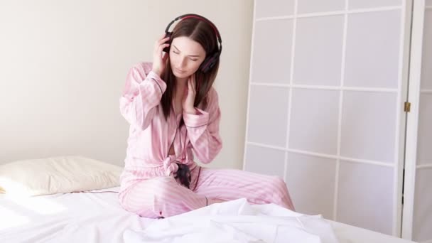 woman in pajamas is lying dances to music from headphones - Footage, Video