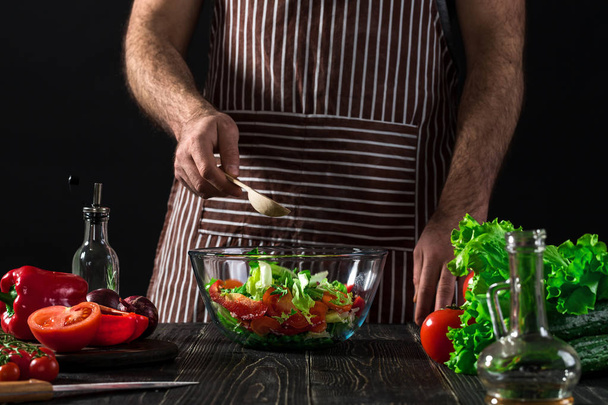 Mies valmistaa salaattia tuoreilla vihanneksilla puupöydällä. Ruoanlaitto maukasta ja terveellistä ruokaa
 - Valokuva, kuva