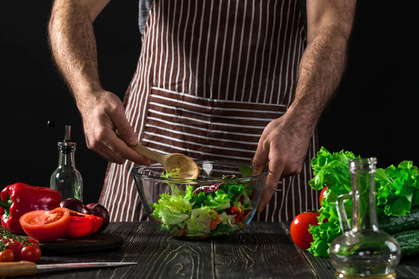 Homem que prepara a salada com verduras frescas em uma mesa de madeira. Cozinhar comida saborosa e saudável
 - Foto, Imagem